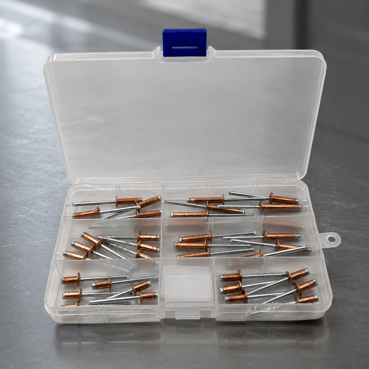 Clear compartment storage boxes filled with copper blind rivets with zinc-plated carbon steel mandrels, shown in a stacked display on a dark premium background.