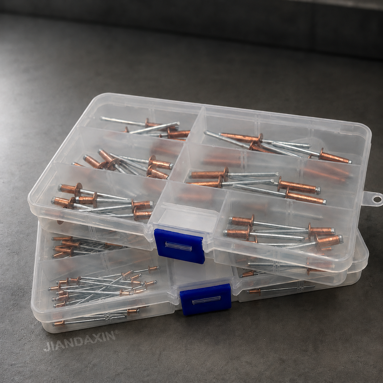 Clear compartment storage boxes filled with copper blind rivets with zinc-plated carbon steel mandrels, shown in a stacked display on a dark premium background.