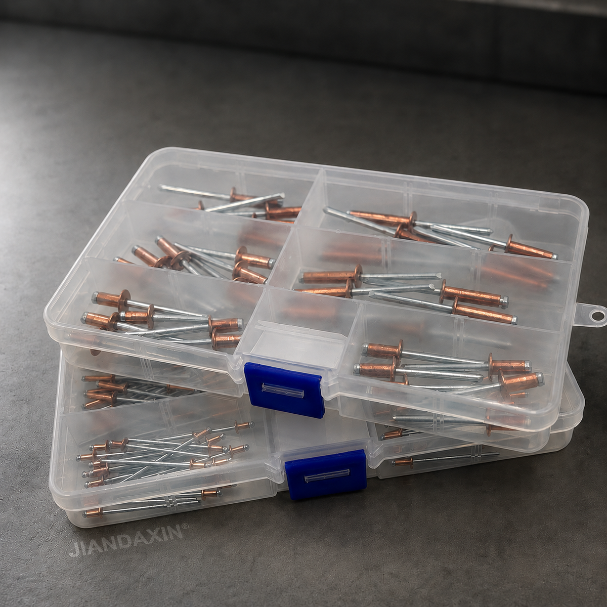 Clear compartment storage boxes filled with copper blind rivets with zinc-plated carbon steel mandrels, shown in a stacked display on a dark premium background.