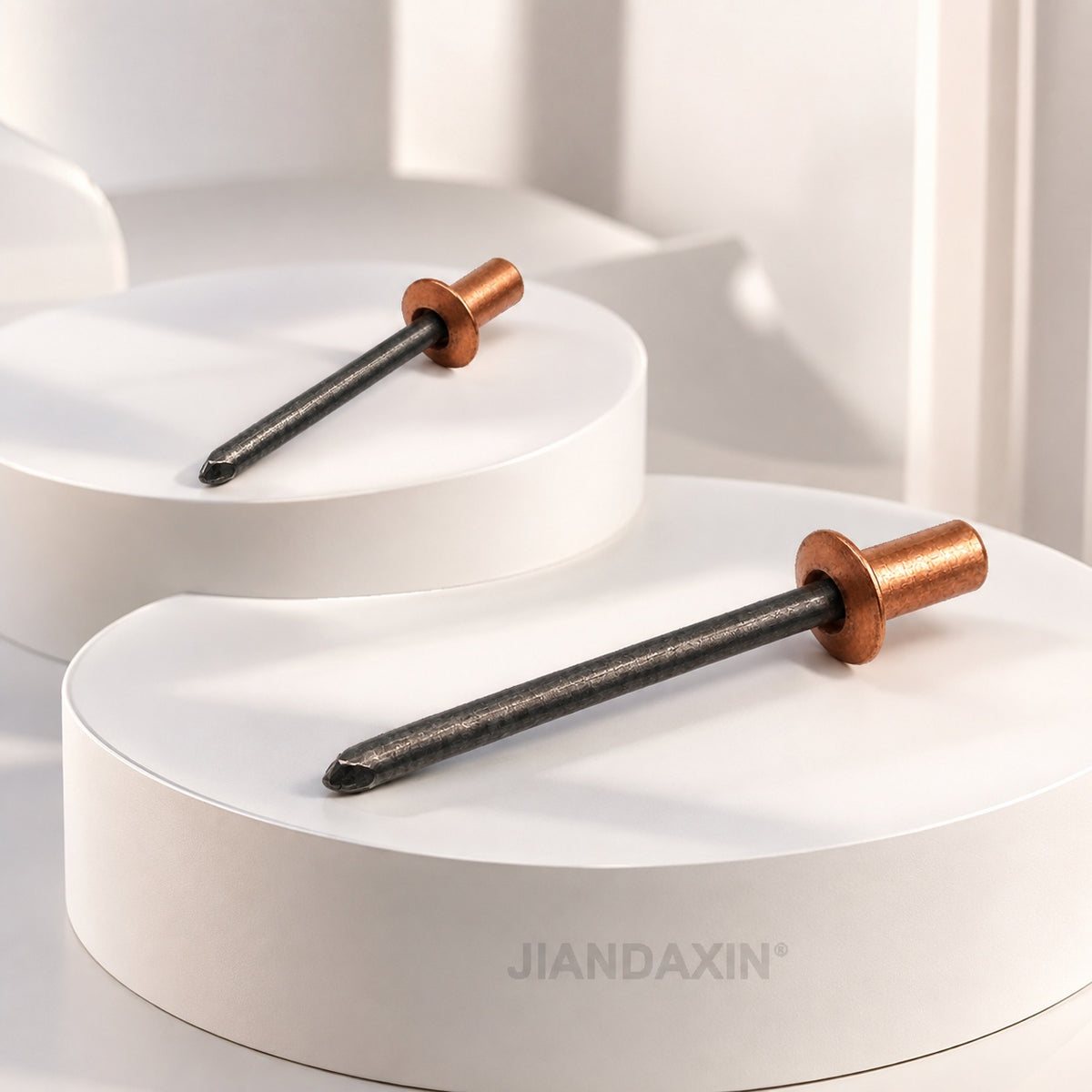 Two closed-end copper blind rivets with steel mandrels rest on layered white display platforms in a bright minimalist setting.