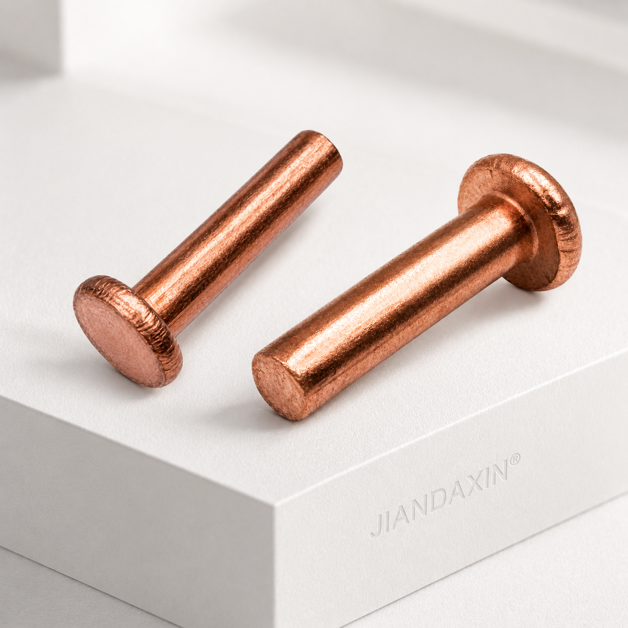 Two copper solid rivets shown from complementary head and tail angles on a bright white platform with soft shadows.
