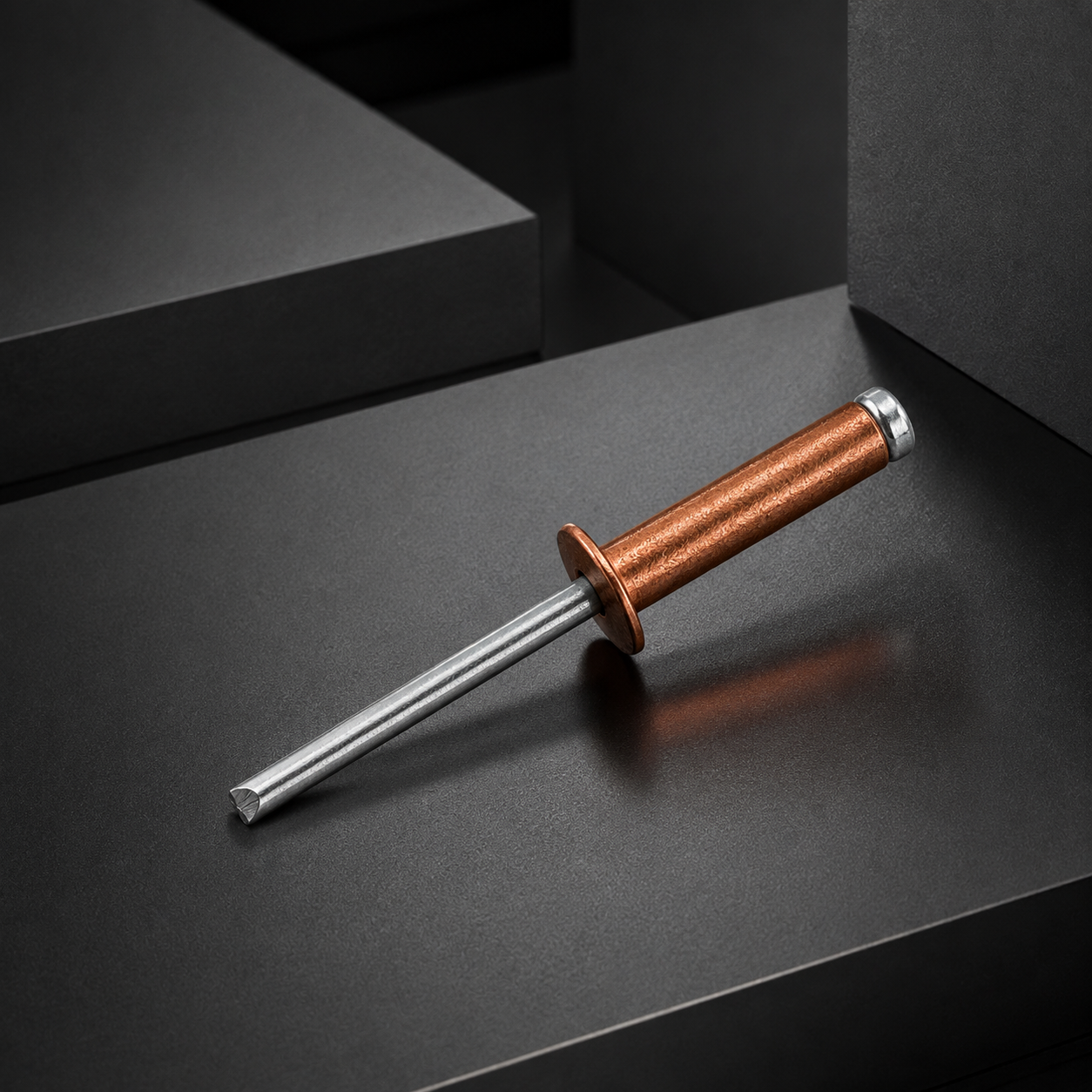 Single red copper open-end blind rivet with a zinc-plated steel mandrel on a dark geometric display stage.